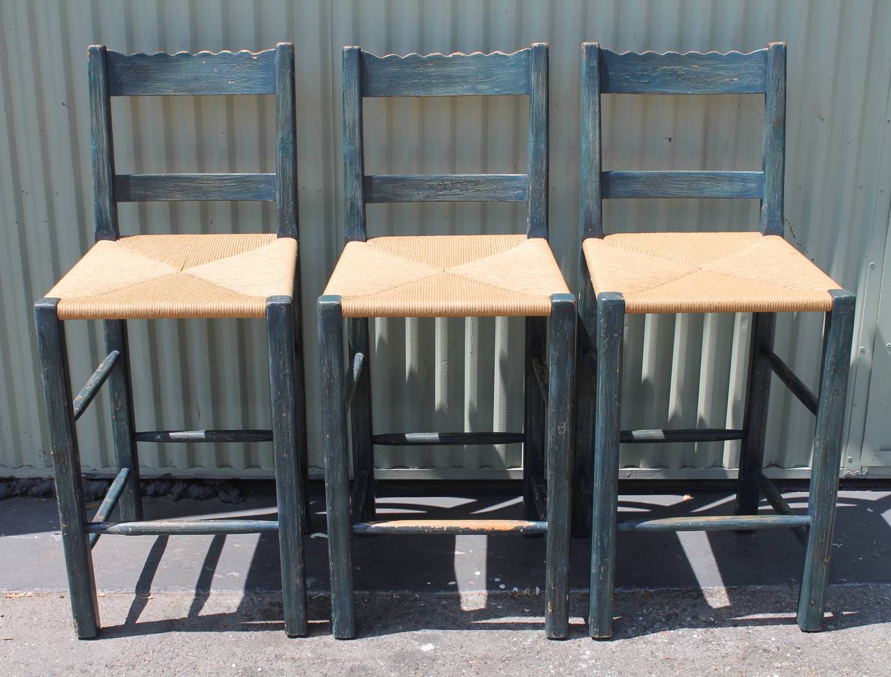 This set of three matching original blue painted handmade bar stools are in good as found condition. The stools are ladder back style with newly hand woven rush seats. Fantastic look for Spanish or country house. They were from a wine cellar or bar