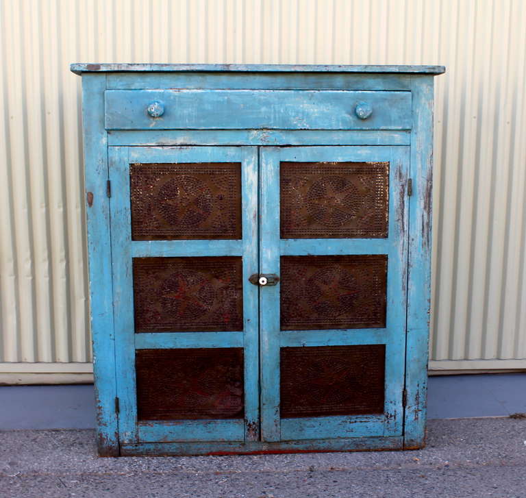 This mid-19th century Pie Safe is in exceptional original untouched condition, showing Robins Egg Blue paint on the exterior and red-wash on the interior. Six ventilation tins with decoratively punched stars and circles are framed three per door.