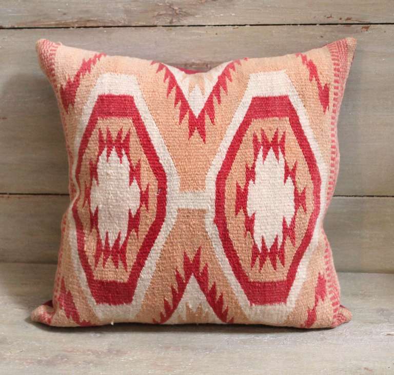 This pillow was constructed from a wide ruins Navajo weaving and dates to the early 1920s. The weaving shows an intricate pattern of triangles bordered in rust, salmon and cream hexagons. The sides are bordered in rust railroad tracked banding. The