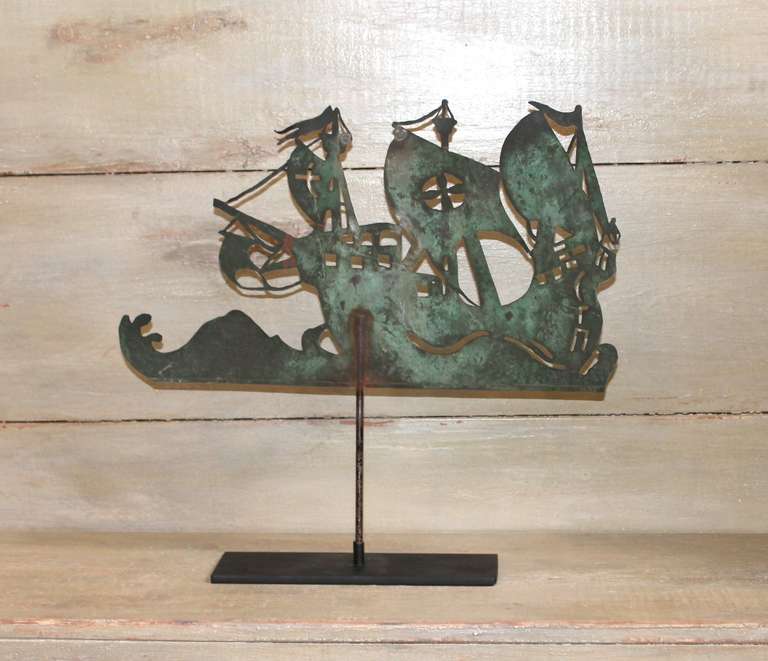 This 19th century New England hand-cut, sheet copper weather vane is fashioned in the shape of a Spanish Galleon and shows waving flags above its decoratively pierced three masts.  The ship is shown sailing through ocean waves and is anchored to a