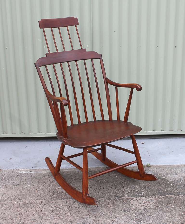This mid-19th century New England pine Windsor rocker shows comb back styling with an extended shawl rack and is in excellent solid condition.  Elegantly simple in stature, the legs are mortised through a solid plank seat showing a rich and warm