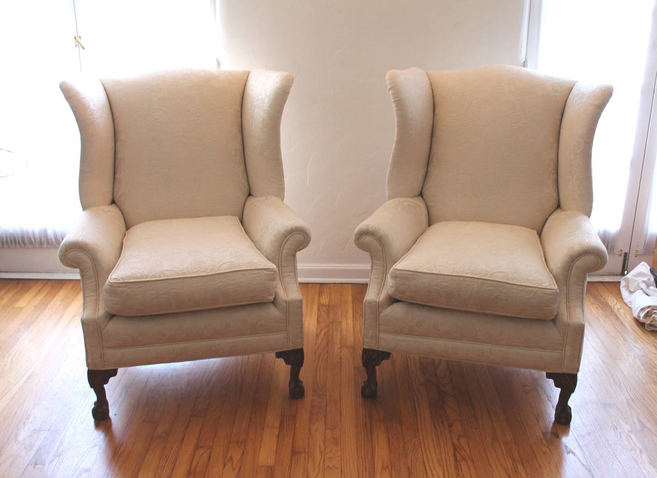 This pair of oversized large wing chairs are upholstered in a wonderful patterned damask cream colored fabric and in fantastic as found condition. The frames are in pine with ball and claw feet with very exaggerated wings. This is one of the best