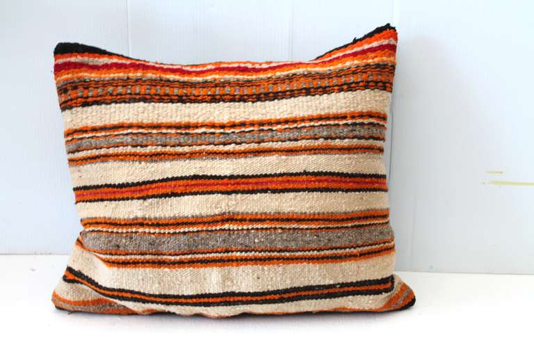 This banded Navajo Indian woven pillow was made from an early saddle blanket and features a combination of homespun native wool and natural wool with aniline dye colors. This piece dates to the early 1900's and utilizes materials and techniques from