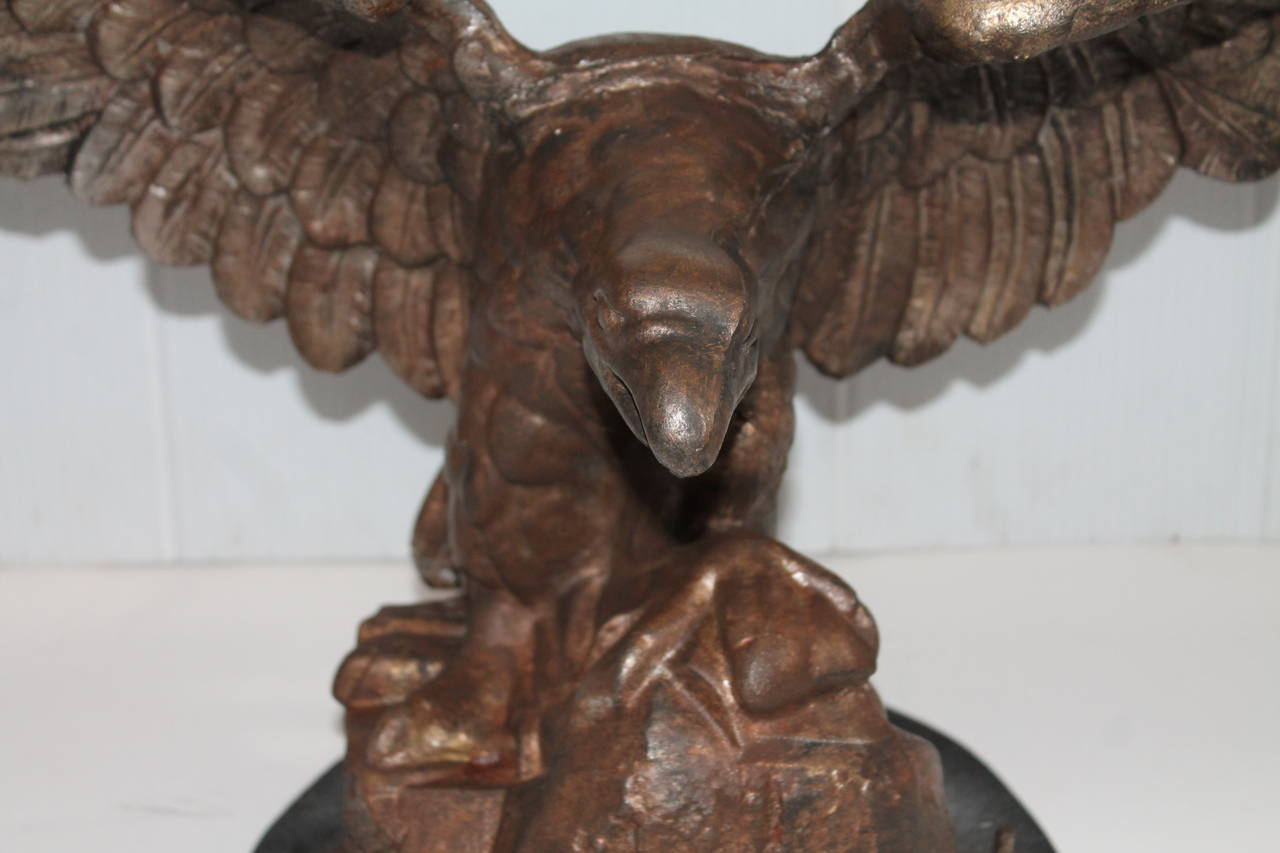 19th century cast iron eagle on a wood base. The base is wood and painted black. This is a very heavy and sits stationary. The eagle is a natural original surface with traces of old gilding.