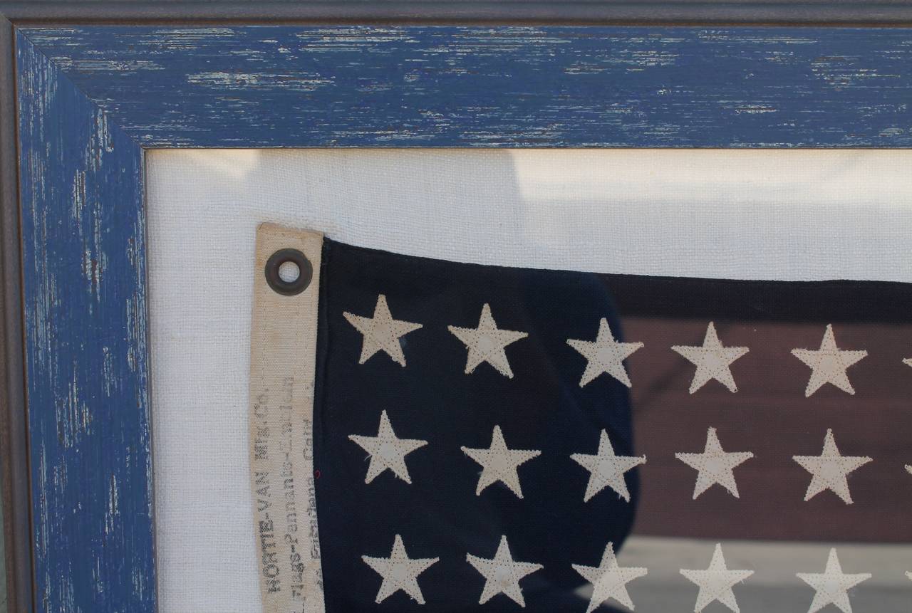 This wonderful 48 star ships flag is hand-sewn on old linen and is in a custom distressed blue painted frame. This is in great condition with a minor, minor moth hole in the lower right hand corner of the flag stripe. This is a diminutive size. The