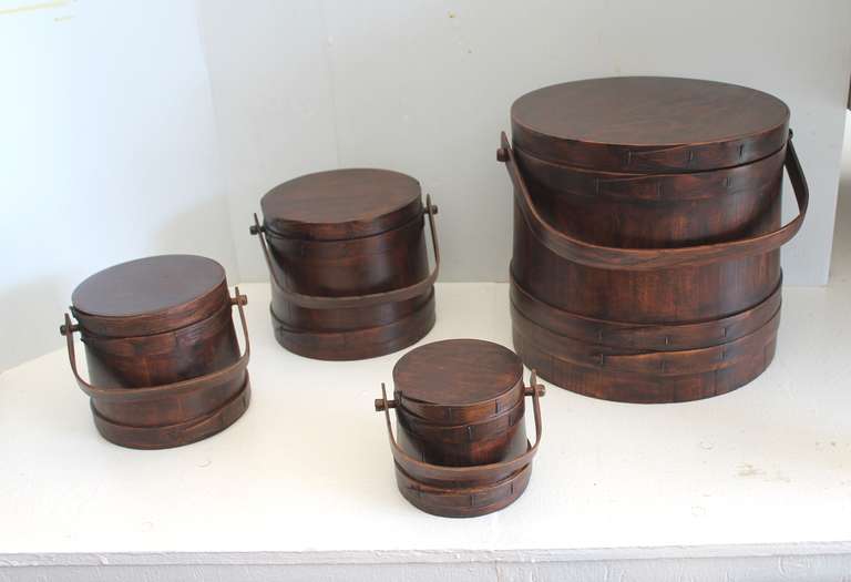 Set of four matching stackable firkins from New England in good condition. These pine buckets have a dark stain surface and are in good condition. Sold as a set of four. Large bucket 12 high x 12 1/2 wide , med.bucket 8 high x 8 wide, next to