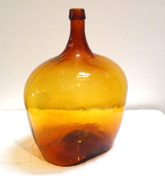 THIS EARLY AND RARE HAND BLOWN AMBER BOTTLE HAS THE MOST WONDERFUL COLOR AND VERY LARGE OVERSIZE SHAPE.THEY ARE CALLED DEMI-JOHNS AND THIS BEAUTY IS FROM NEW ENGLAND.FANTASTIC CONDITION AND A VERY LARGE PONTIL ON THE BASE.