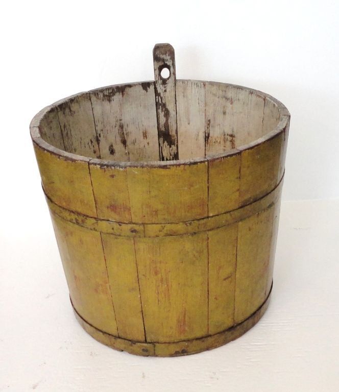 19THC ORIGINAL MUSTARD PAINTED EXTERIOR AND WHITE WASHED PAINTED INTERIOR WATER BUCKET.THIS WONDERFUL COLORED AND RARE WATER OR SAP BUCKET IS FROM NEW HAMPSHIRE .IT RETAINS THE ORIGINAL METAL BANDS AND WOOD HANGER WITH A HOLE FOR HANGING.IT IS SO