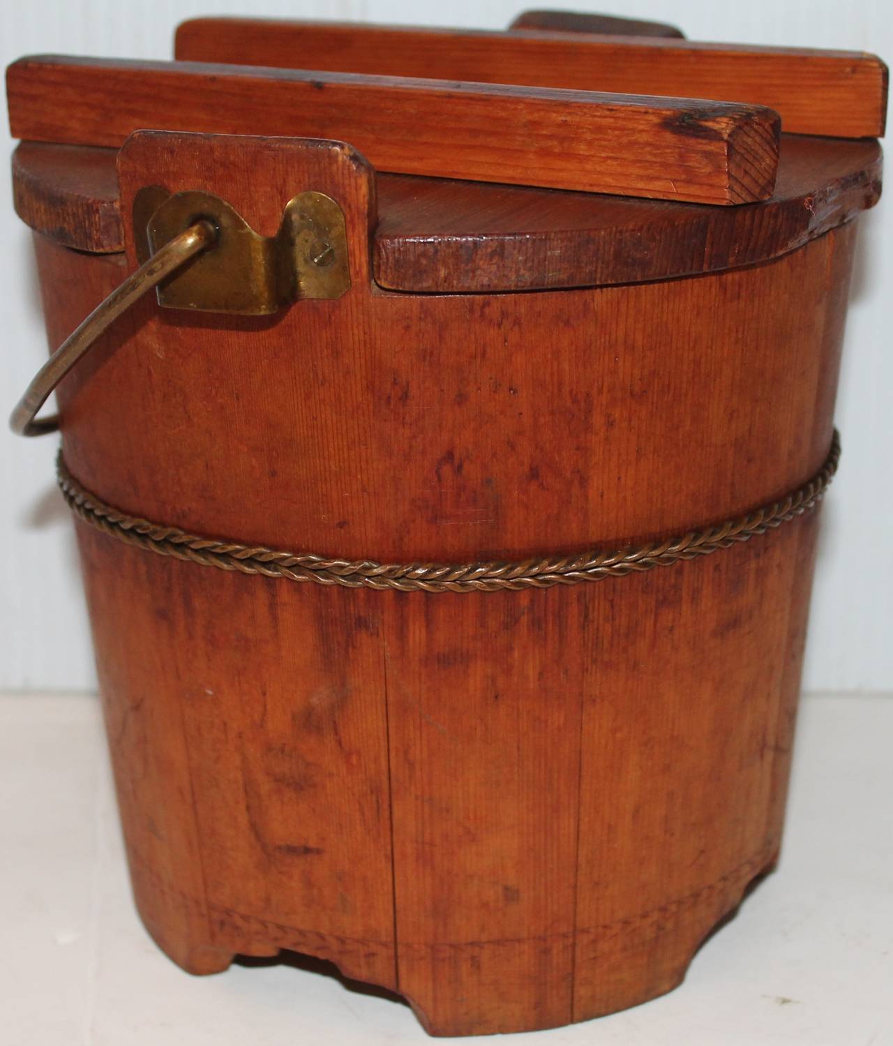 This unusual 19th century pine sugar or grain bucket has the original metal handle and twisted metal trim. The base has very unique cut-out throughout. The lid is original to the piece. The piece is in very good condition.