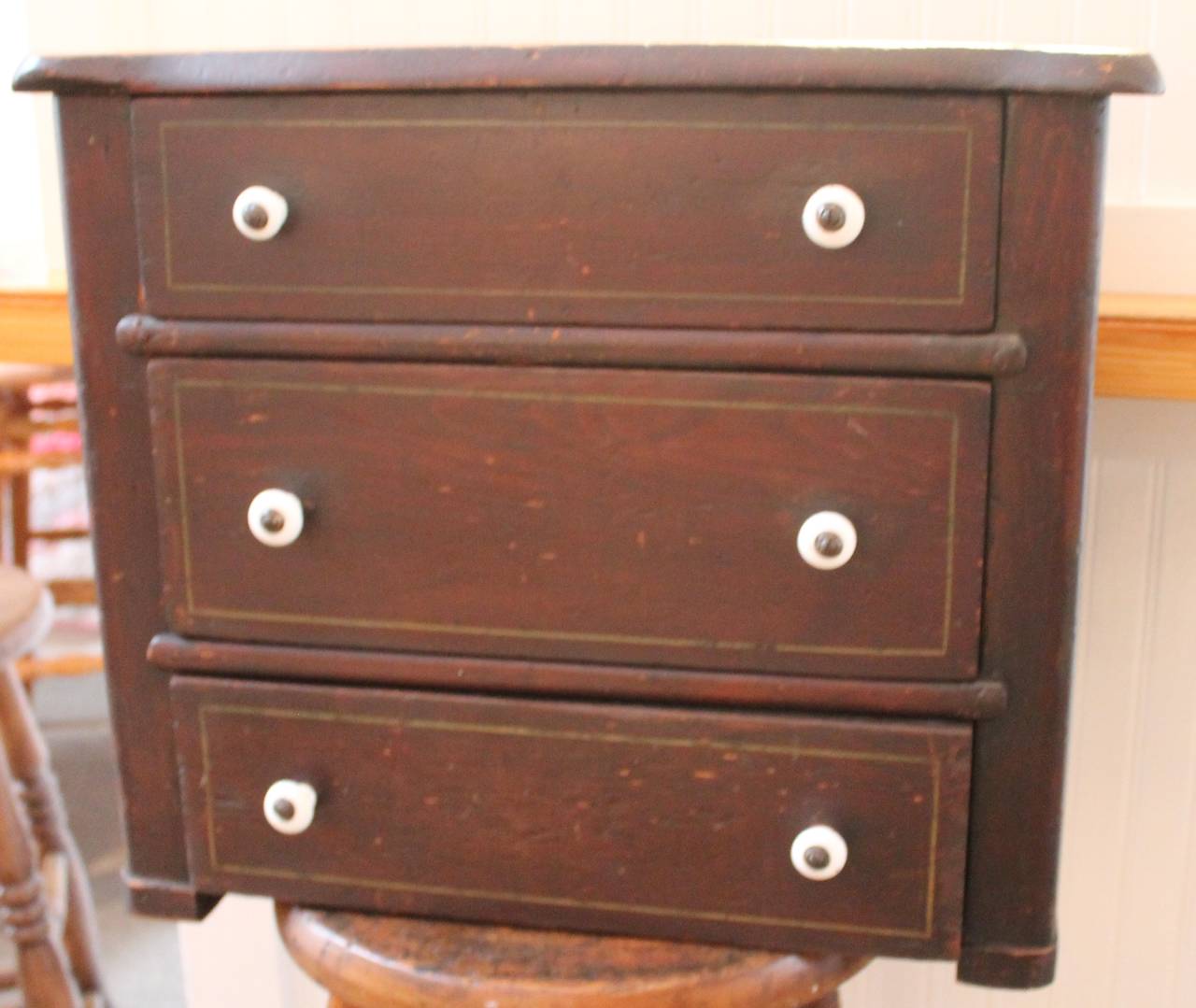 19th century original stained chest of drawers with original gilded trim. The porcelain knobs or drawer pulls are also original to the miniature chest of drawers. The construction is all square cut nails. This would make a wonderful counter spice