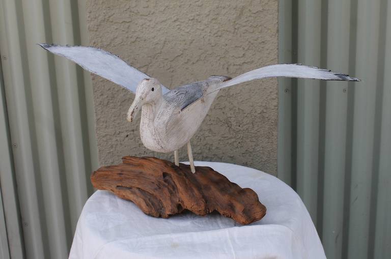This wonderful folk art bird was found in the state of Maine and is hand carved wood with original painted tin wings. This fine sculpture is most interesting with the original painted tin wing span.The drift wood piece seems to be original to the