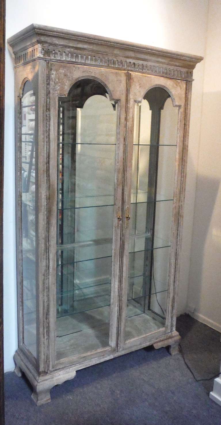 This impressive heavy beveled glass-paned display cabinet stands 7 feet 7 inches in height and features beautifully distressed detailing with OG feet.  Classically French in design, this piece has had added recessed lighting for purposes of