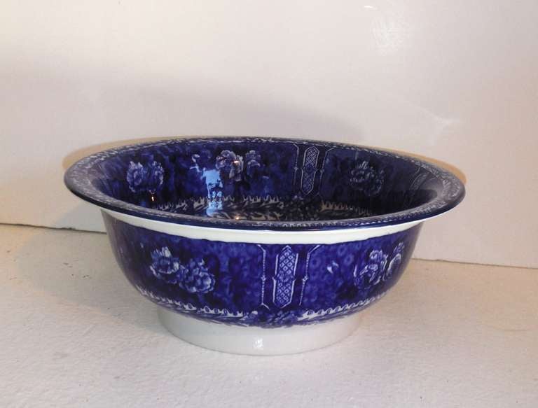 This historical flow blue bowl in a Sylvan pattern, circa 1930, shows a stunningly rich scenic interior of a riverside park, sailing vessels and antiquated architectural reference.  The exterior of the bowl is highly decorated in cobalt blue roses,