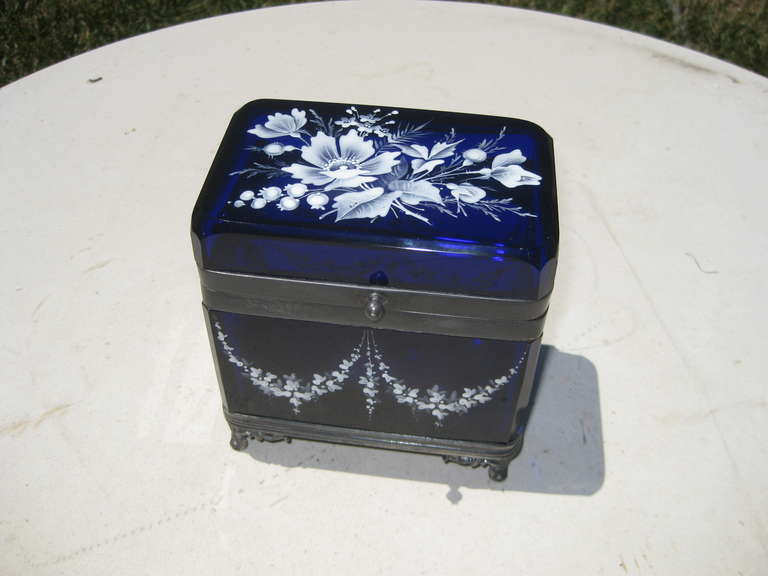 Beautiful cobalt blue glass box with metal mounted rim and footed base and white enamel decoration.