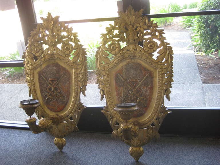 Pair of large caved shield back wall plaques with candle sconce arms.  These are made to look like they are 18th Century but they are 20th C Italian reproductions for the tourist trade.  The giltwood and silvered finish is excellent along with the
