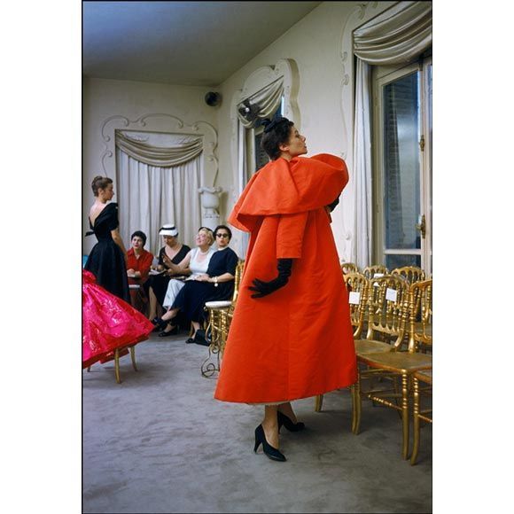 A magical moment is captured by photographer Mark Shaw in the salon of Balenciaga in Paris in 1954. Here a model poses for American buyers from I Magnin department store in Balenciaga's signature Orange Coat. This image is an outtake from an