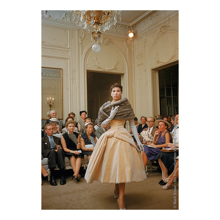 Photographed by legendary photographer Mark Shaw at the salon of Christian Dior in 1954 is a model wearing a cream velvet tea length gown. Buyers and other important guests look on. This image is an outtake from an assignment for LIFE magazine shot