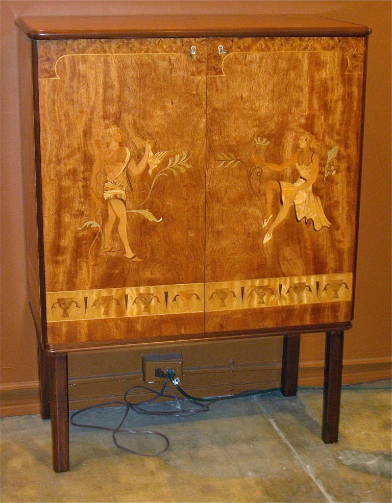 Extraordinary Swedish art deco/neo-classical inlaid storage cabinet. Rendered in satin wood, carpathian elm, golden flame birch and mahogany. Made at Mjolby Intarsia company in Southern Sweden in 1940. Interior is composed of adjustable/removable