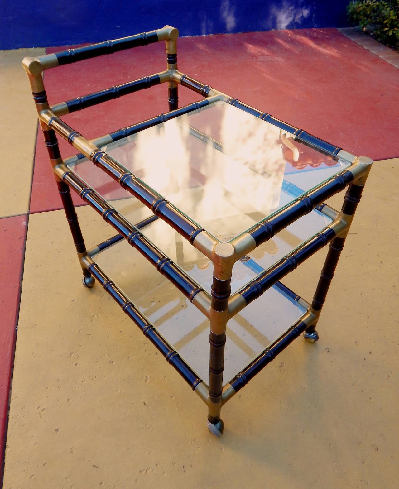 Argentine mid-20th century modern bamboo bar cart in ebonized hardwood and bronze. Three serving shelves are fitted with polished glass. Original metal casters.