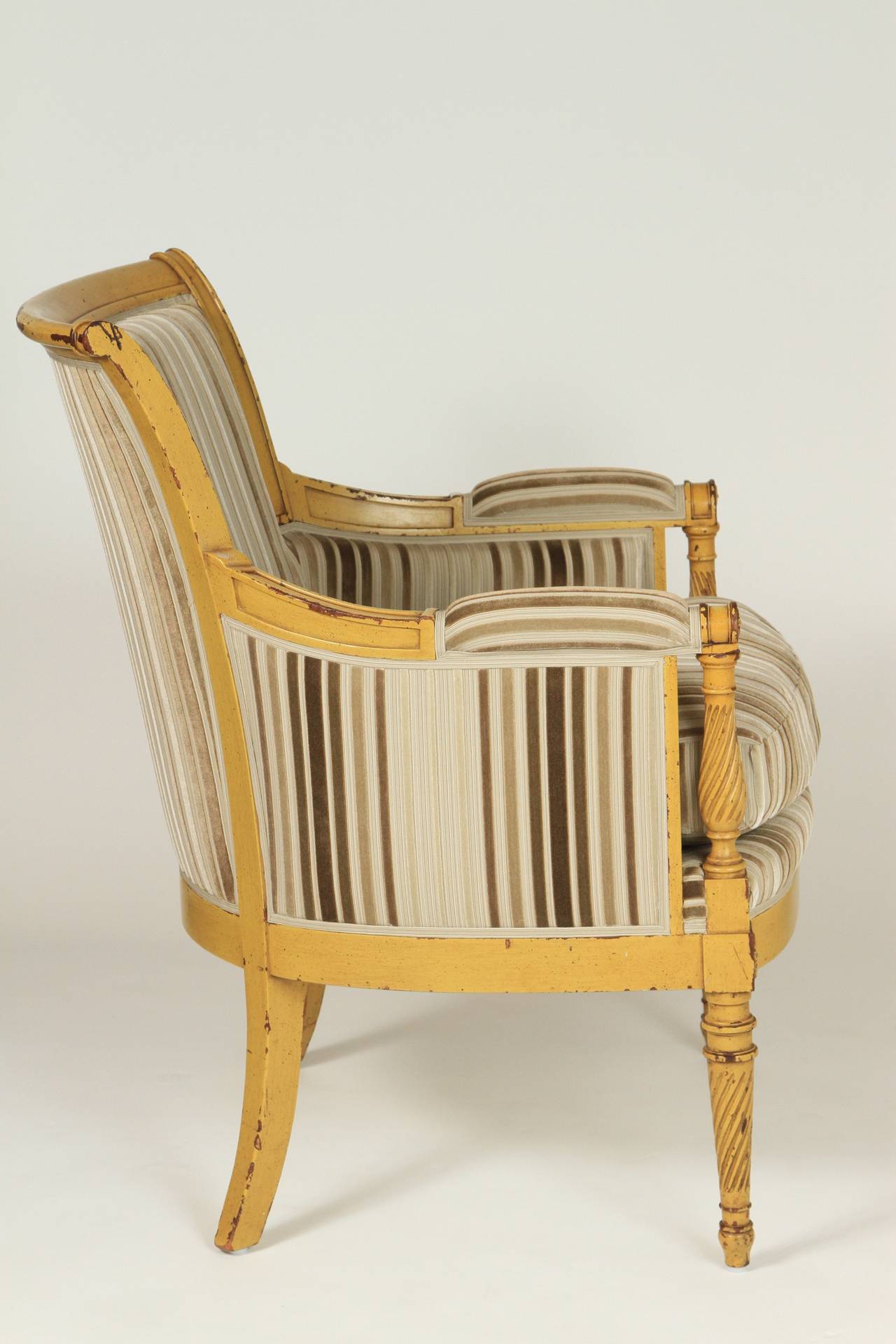 Stylish pair of Bergere chairs. Newly upholstered in silk with cut velvet striping. Yellow painted frames are original and are nicely worn, which lends depth to the chairs' character. Down and feather cushions add to their luxury.