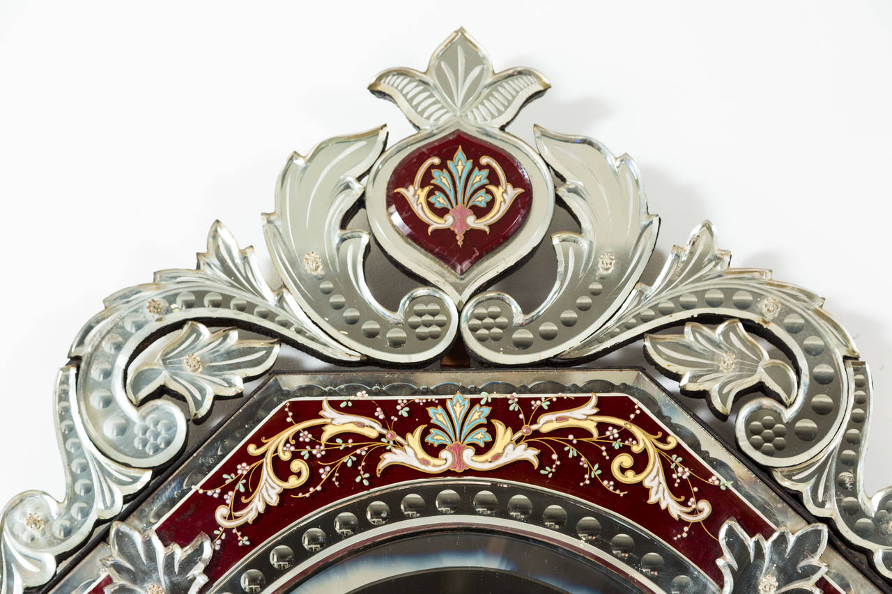 Truly elegant Venetian mirror with an incredible amount of ornate detailing in the Baroque Revival style. Hand painted floral motifs in enamel accent the frame, which is a rich burgundy color. The mirror itself is nicely beveled and in excellent,