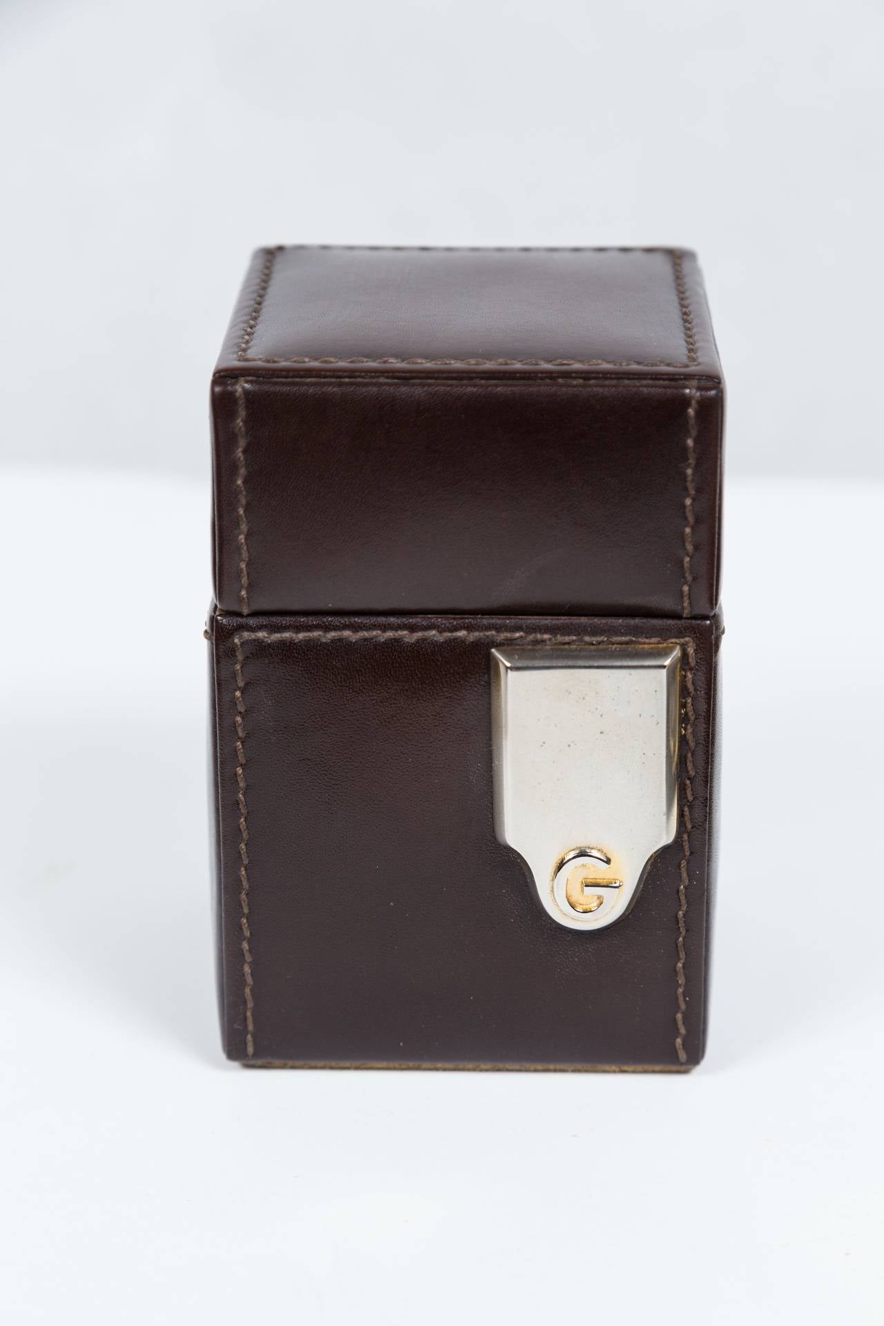 Handsome set features a writing pad, lighter and cigarette box lined in Mahogany with a center divider. All in excellent condition. Pieces are clad in brown leather with suede undersides and feature metal mounts with the 