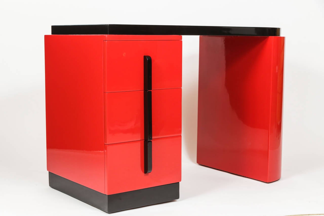 Stunning small desk with attributes of Gilbert Rohde's design work, seen in the rounded shape and vertically stylized drawer handles. Desk has just been restored in polished red and black lacquer and features a black leather top. There is side