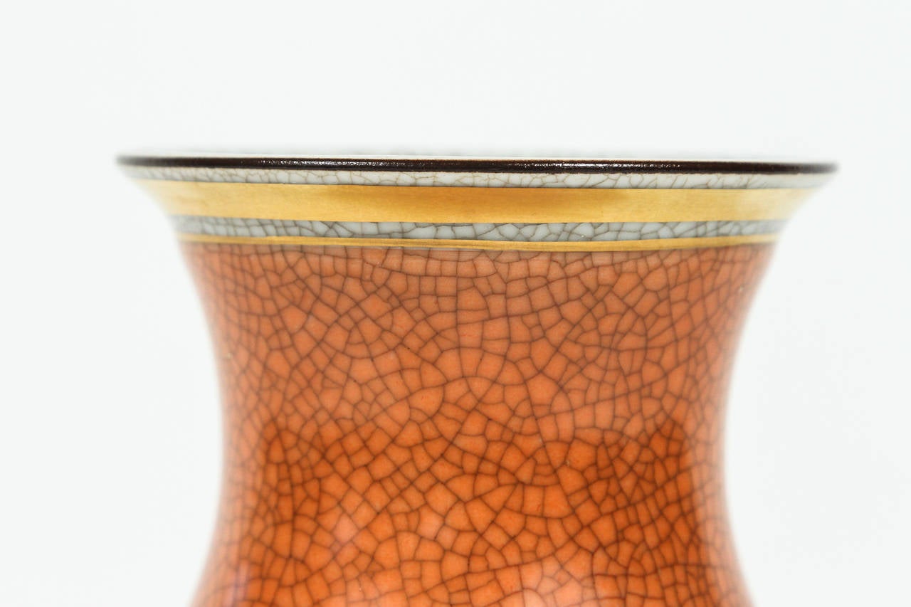 Graceful, small ceramic vase with an orange raku glaze and a neutral gray raku glaze interior. It is accented by hand-painted gold leaf around the top and bottom. A brown hand-painted glaze surrounds the top. Stamped on the underside: 