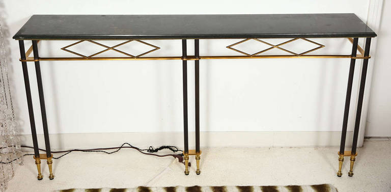 An elegant doré bronze and antique brass console table with a green marble top by Jules Leleu. The console table has three pairs of fluted legs along the front and a decorative diamond pattern apron front detail. The console anchors to the wall at