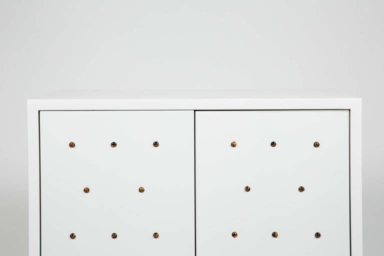 A chic cabinet in white lacquer studded with tigers eye cabochons and with walnut stained feet. The cabinet also features touch latch hardware and a single drawer inside. This piece can be customized in the color of your choice as we as gem stones.