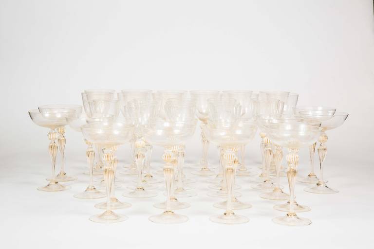 A beautiful set of Venetian stemware, by Barovier, with clear bowls and stems with gold inclusions, and ribbed white glass knobs under the bowl. This set is comprised of twelve red wine,  white wine and coupes.  There are an additional 2 coupes.  