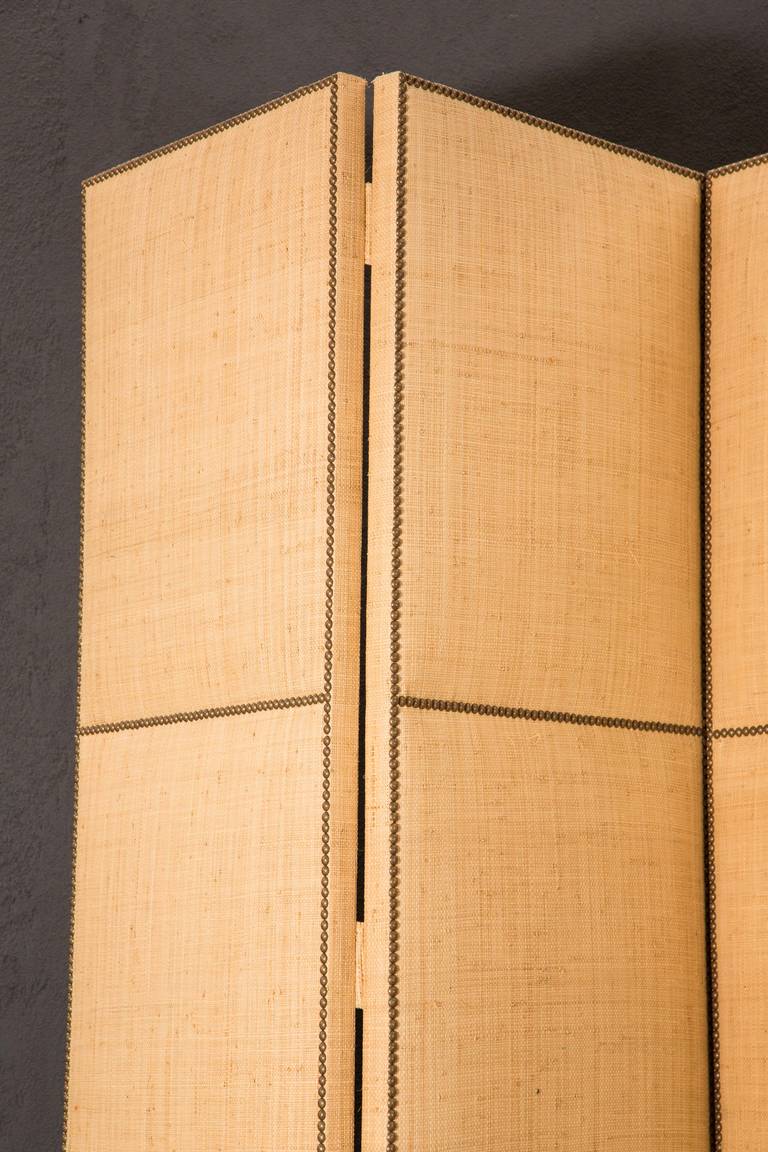 A custom made nine foot tall raffia-upholstered screen with nailhead paneling detail. This screen is currently separated into three two-panel sections for ease of transport and has tabs for easy reattachment as hinges (see Image 8). Each panel