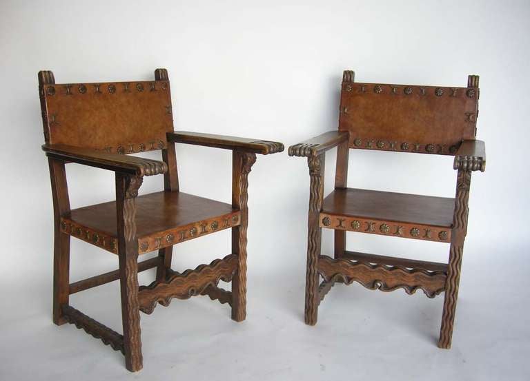 Pair of carved antique leather arm chairs in very good condition. Very comfortable and sturdy. Very interesting brass nail heads all around.