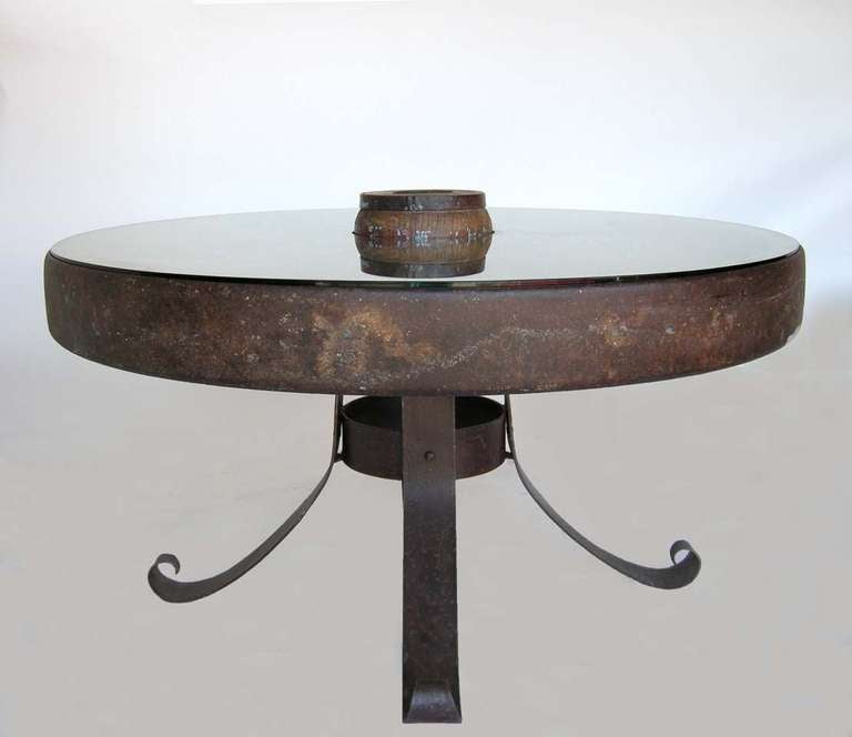 Wheel table consisting of 19th c. iron wheel with wooden spokes atop contemporary hand forged iron base and glass top. 
Distance from floor to apron is 24.75 inches