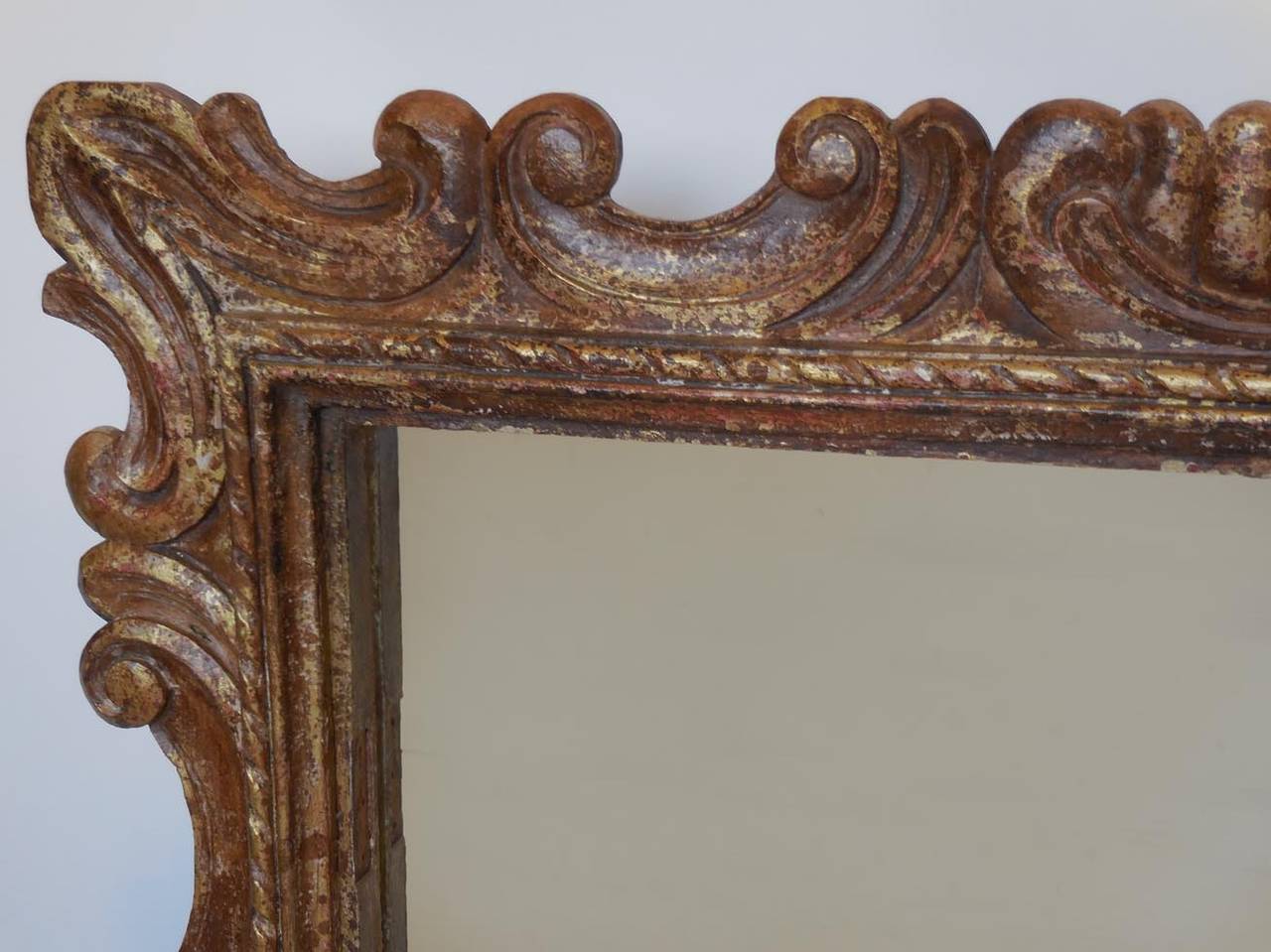 Hand-carved hardwood frame around clear mirror glass. Gesso and hand-painted in variations of gold tones.