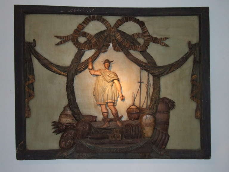 An 18th century trade sign from a Dutch East Indies shipping merchant.  The carved and polychromed sign depicts a winged-foot mercury surrounded by garlands with his ship and the wares of a merchant at his feet.  Such a sign would at one time have