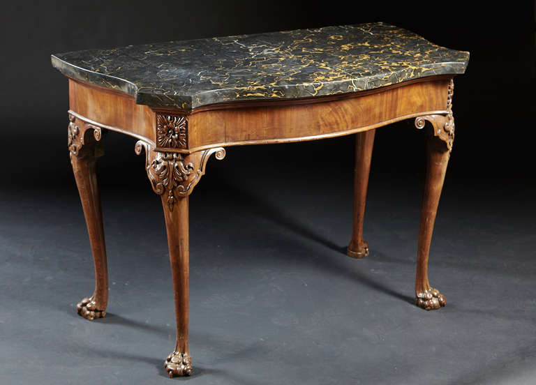 A George II marble top serpentine console table with cabriole legs ending in lion paw feet. The original thick, chiseled black and gold porto marble rests on a conforming serpentine frame with canted corners having carved rosettes and acanthus