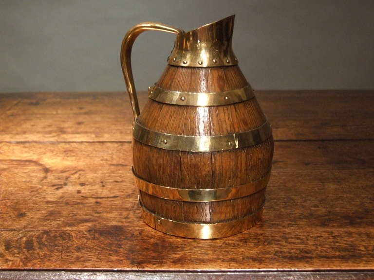 Charming English 19th Century cider jug of staved and banded construction, the graduated brass bands and pouring spout mounted with studded brass pins, the shaped handle wrought of fruitwood clad in brass and the whole with pleasing mellow surface.
