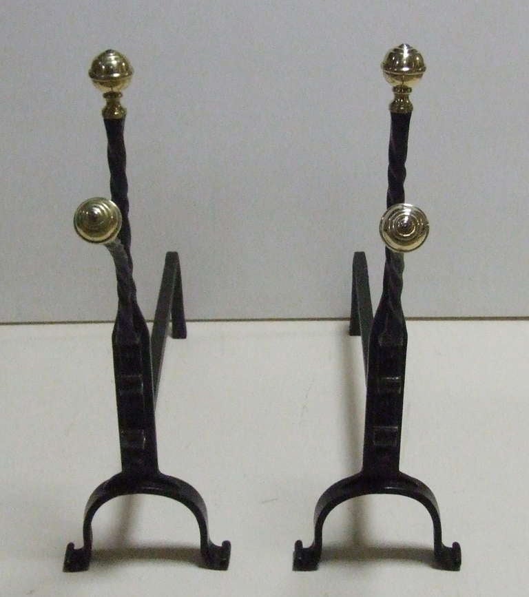 Charming pair of brass and wrought iron andirons, the ringed ball finials over barley twist shafts, the front finials having exaggerated projecting stance, also with barley twisting, standing on arched legs ending in scrolled feet.
 