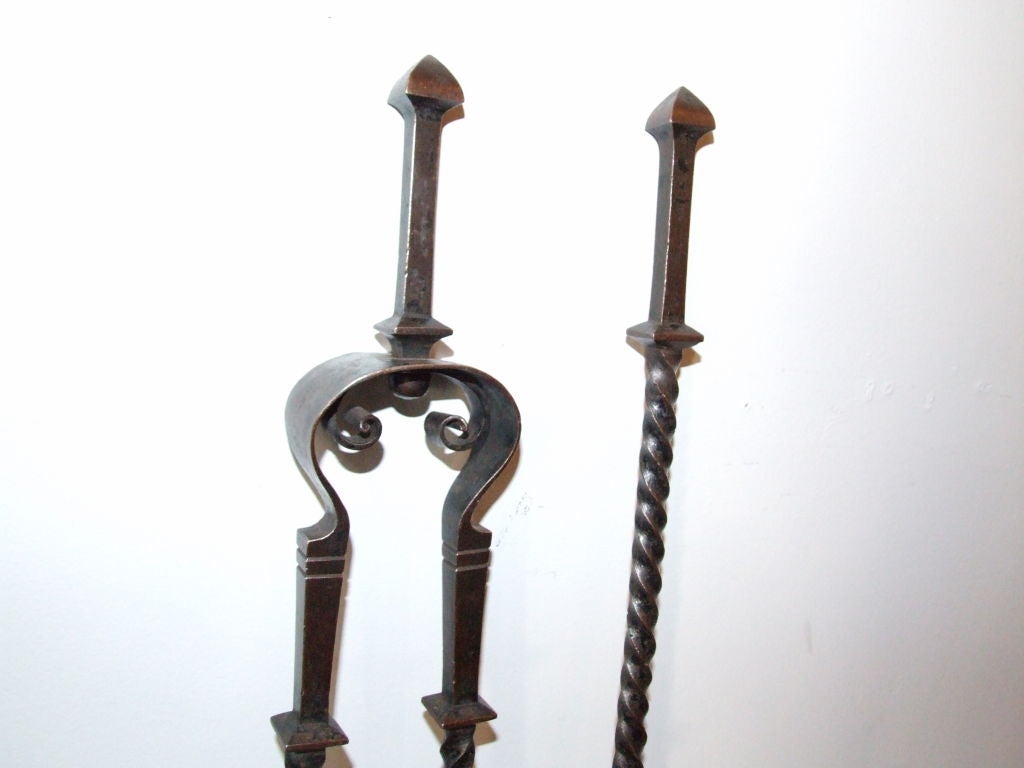 A pair of tall fire tools in blackened wrought iron comprising a pair of tongs and a poker having partially twisted shafts and shaped finials with scrolls to tongs in heavy gauge wrought iron.