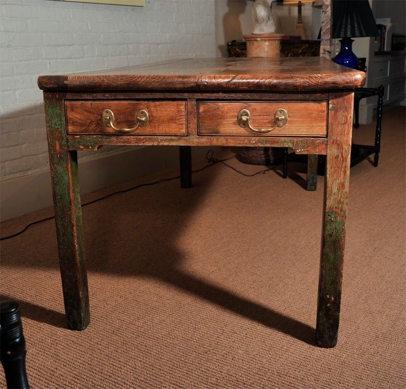A mid-19th century English green painted and elm country farm table/desk with a nicely figured elm top over a frieze and raised on four square legs. The frieze and legs bear traces of green paint. The frieze is fitted with two drawers on one end