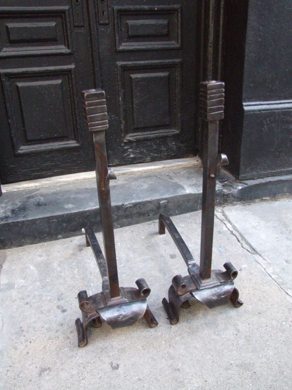 Bold pair of 19th c wrought iron andirons with ribbed rectangular finials over squared shafts with 'S' scroll supports over heavily scrolled and weighty base.