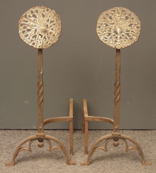 A pair of Aesthetic Movement andirons with twisted wrought iron shafts, shaped horseshoe feet and pierced stylized peacock pierced brass roundels.