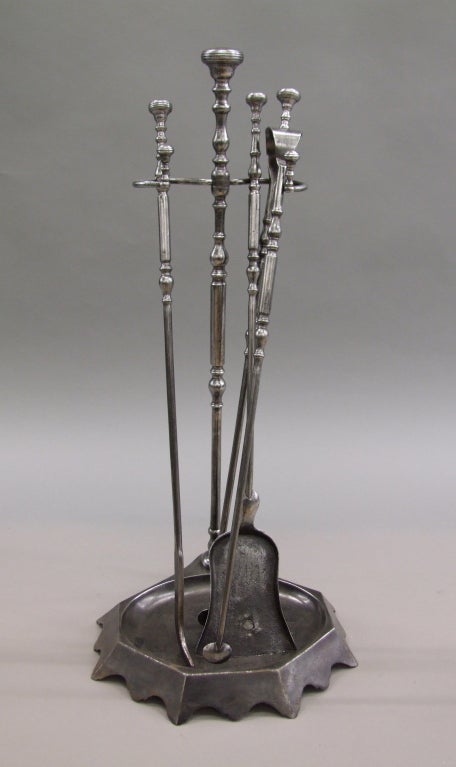 Set of three steel fire tools with original stand, the ringed button handles over turned shafts with balustrade turnings, comprising shovel, tongs and hooked poker, the stand with scalloped flared base.