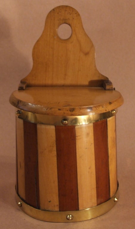 Ravissante boîte à sel écossaise du milieu du 19e siècle, montée sur un mur et construite en bois, avec un dos en forme et un couvercle à charnière sur un corps demi-rond en bois mélangé, relié en laiton avec des rivets d'origine.
 
Treen