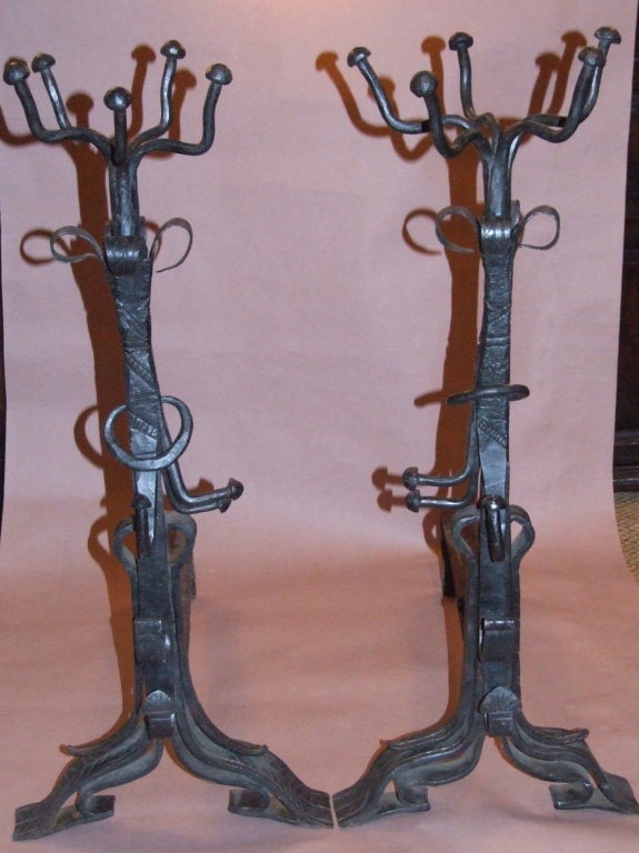 An impressive and unusual pair of Arts and Crafts wrought iron andirons in the manner of Samuel Yellin, the open basket finials with mushroom capped ends, over rustically wrought shafts having mushroom finial hooks, ring loops and chevron spit