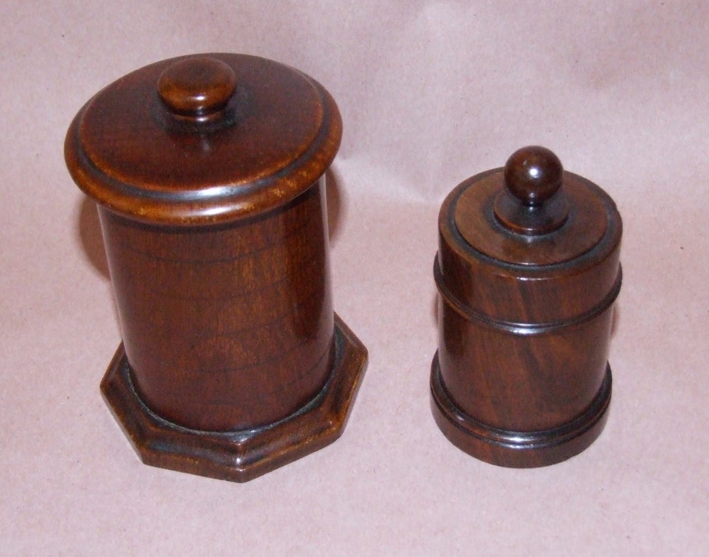 Two English 19th Century turned wooden boxes, the taller fashioned in oak, with ringed body and octagonal base, the shorter in walnut with turned ball finial, cylindrical body and stepped turned base, both with good color.