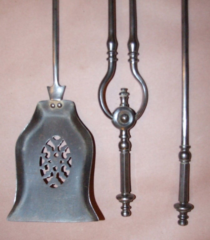 Set of simple 19th Century English steel fire tools comprising a poker, tongs and shovel, the later with pierced lace design, the handles with ball finials over octagonal grips, all in good gunmetal finish.