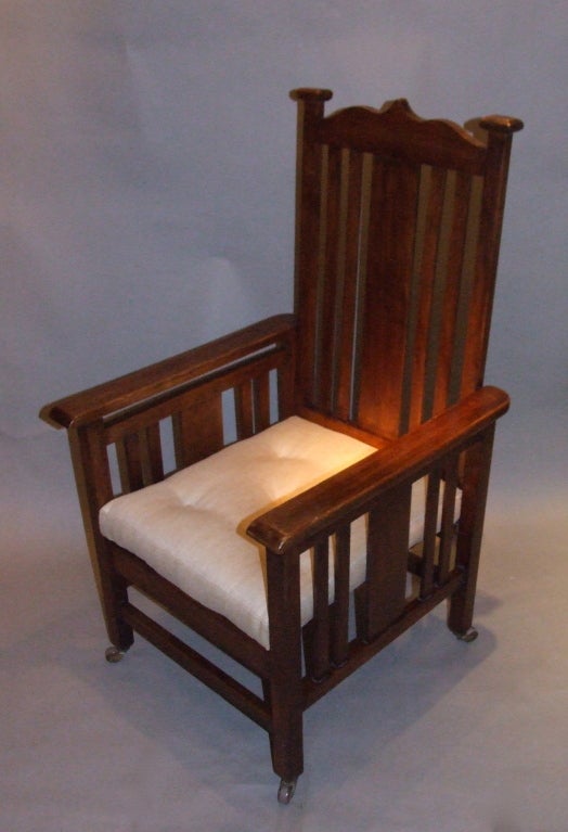 English Arts and Crafts period armchair, the shaped crest over slatted back, the arms similarly slatted, standing on square legs on original brass and ceramic castors, the upholstered cushion with shallow button tufting, the whole with good mellow