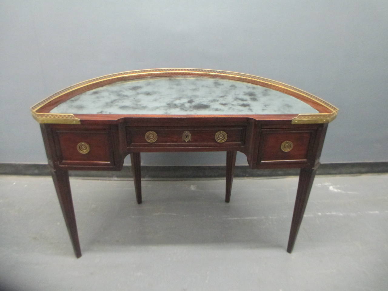 Demilune Louis XVI style mirrored-top writing desk with brass gallery on tapered fluted legs.

Price reduced/net price $5,500.